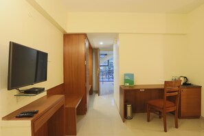 A hotel room with a TV, a desk, a chair, a trash bin, and a view of a balcony. - Hotel Mint Highstreet (Pune)