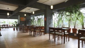 A spacious indoor area with tiled flooring, wooden tables and chairs, potted plants, and large windows allowing natural light. - Hotel Mint Highstreet (Pune)
