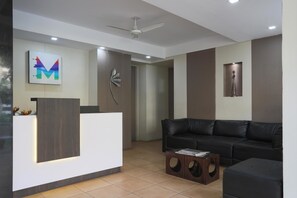 A modern reception area with a white reception desk, a black leather sofa, and a decorative wall piece. - Hotel Mint Highstreet (Pune)