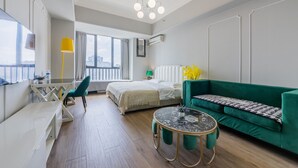 A modern hotel room with a bed, green sofa, a small round table, and a desk with a chair. - Lavender Apartment -Wanda Branch (Guangzhou)