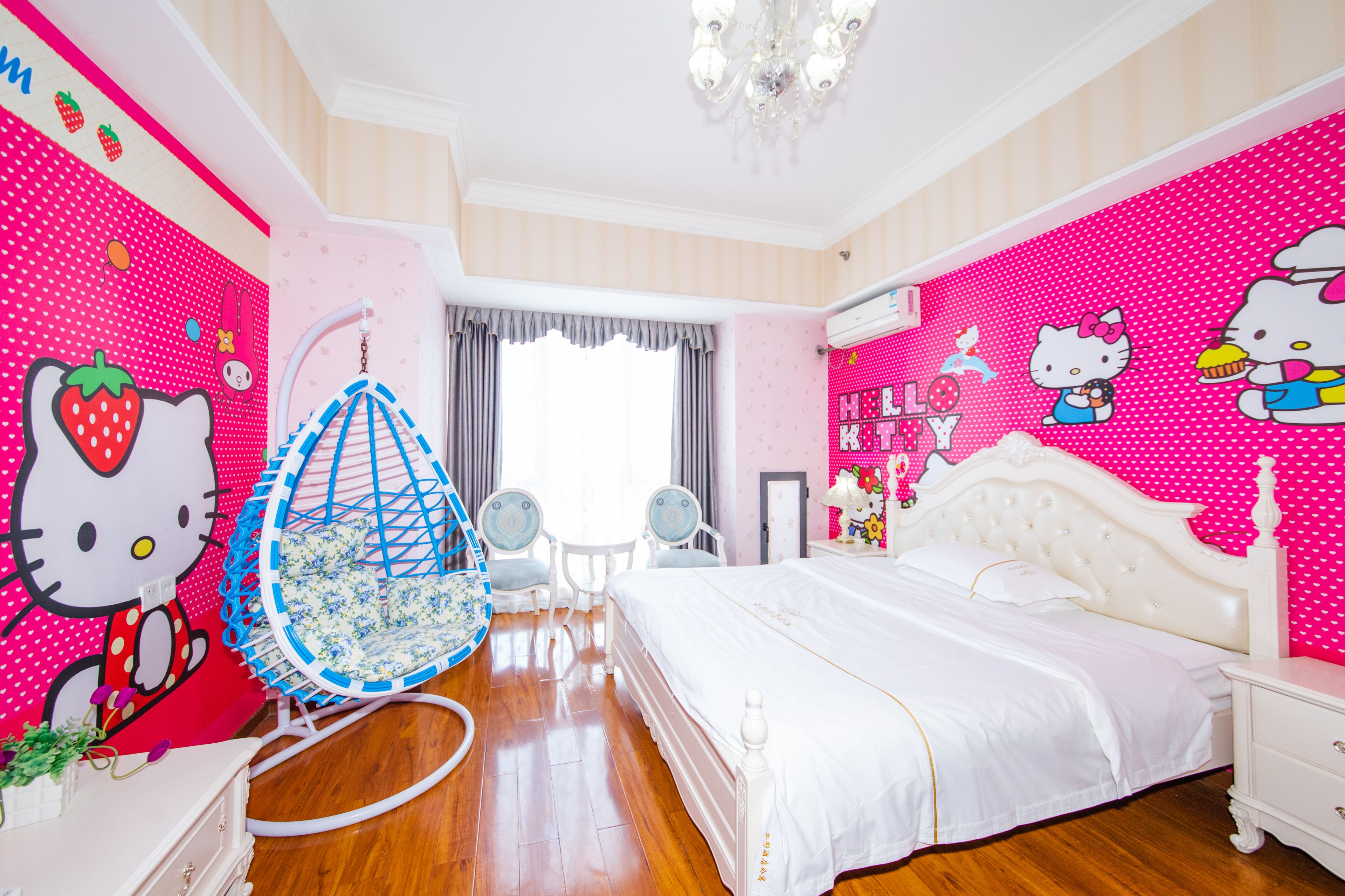 Ein Zimmer mit einem Bett, einem Hängesessel und einer Wand, die mit Hello Kitty Figuren verziert ist.