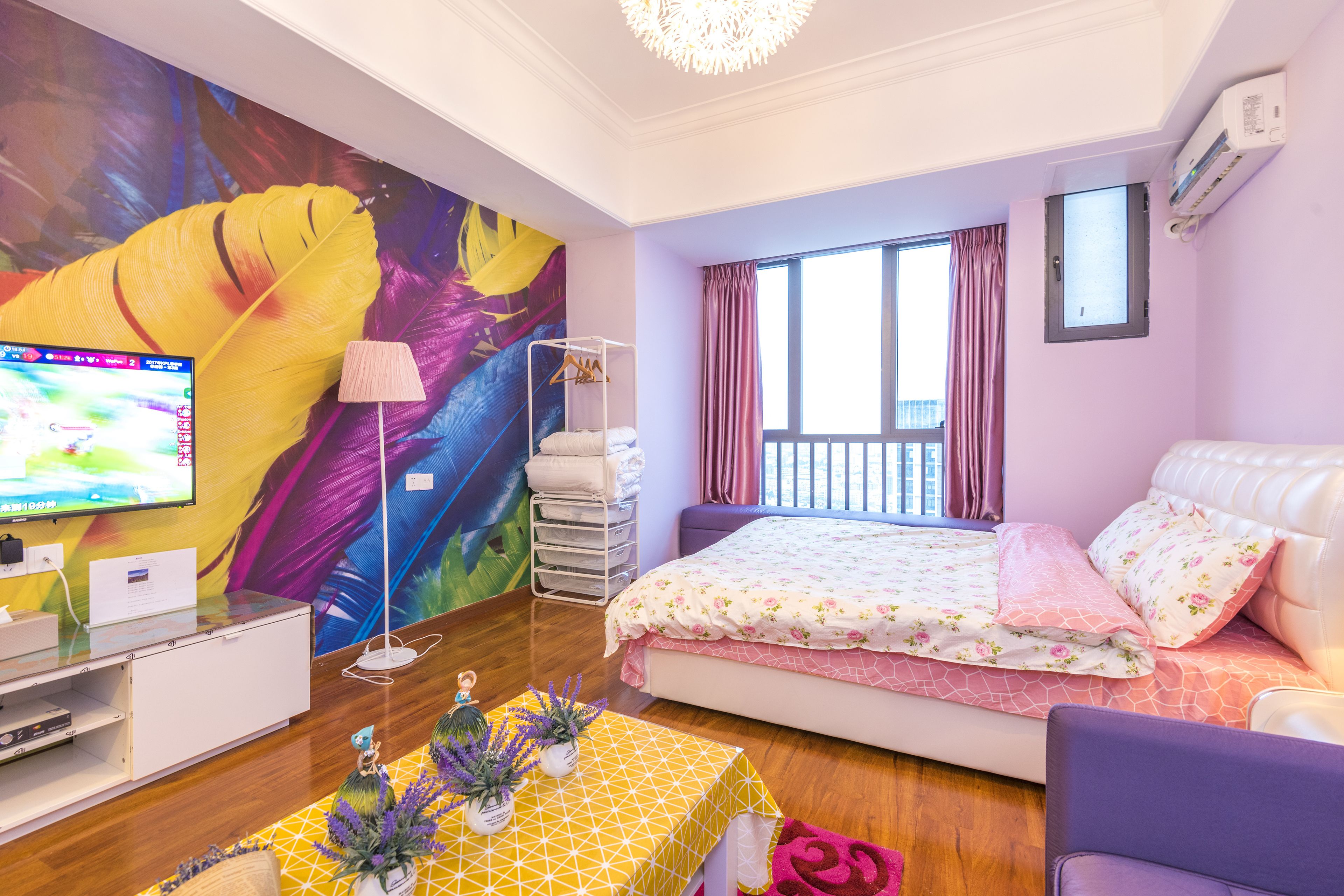 A hotel room with a bed, a TV, a desk, and a colorful mural on the wall.