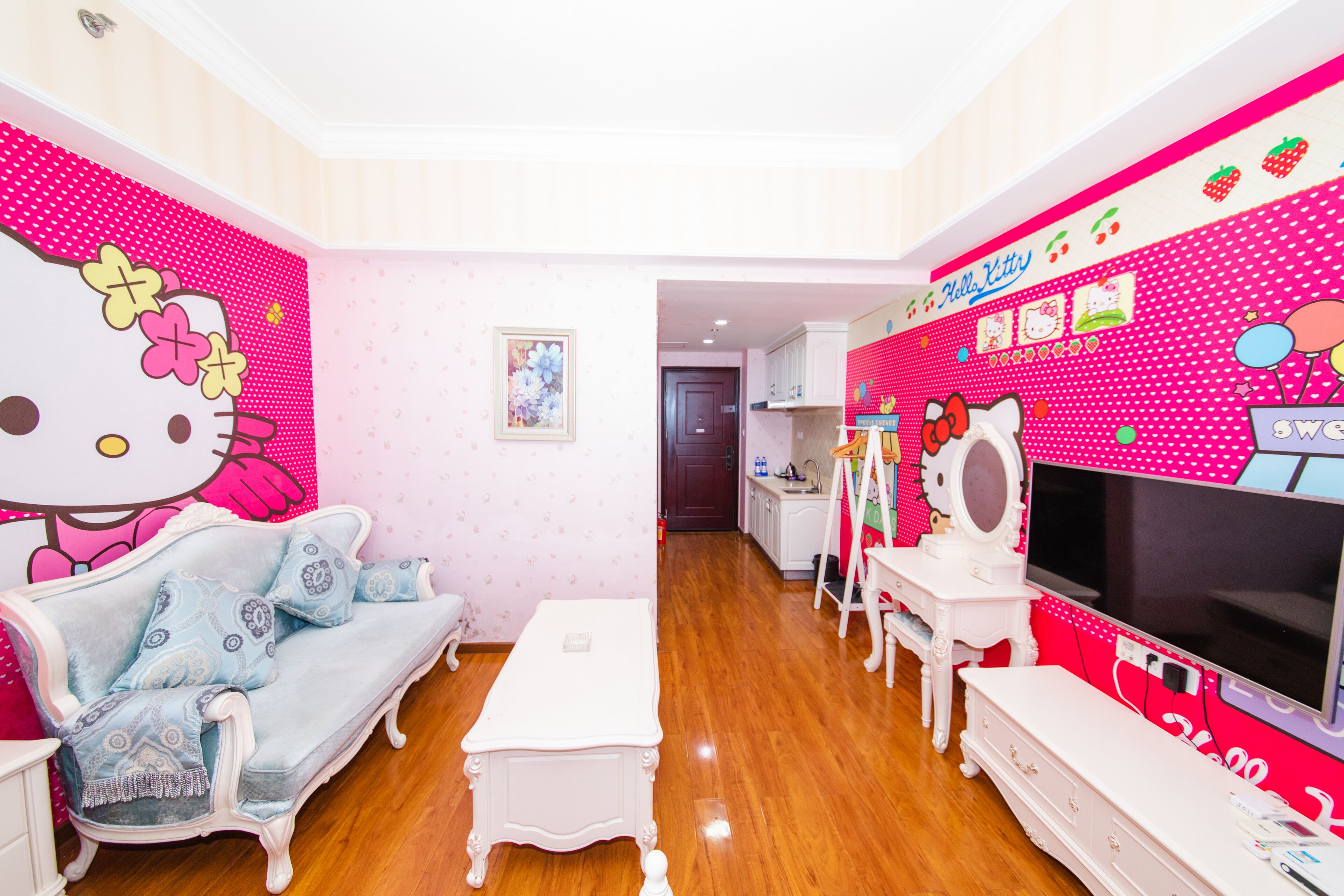 A room with a blue sofa, white coffee table, and a pink wall with Hello Kitty decorations.