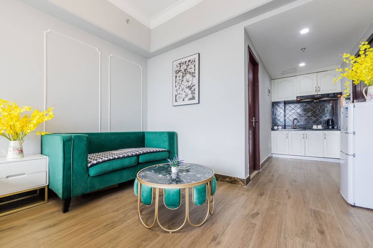 A modern living room with a green sofa, a round coffee table, and a kitchen in the background.