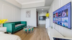 A modern living room with a green sofa, a round coffee table, and a flat-screen TV displaying a movie. - Lavender Apartment -Wanda Branch (Guangzhou)