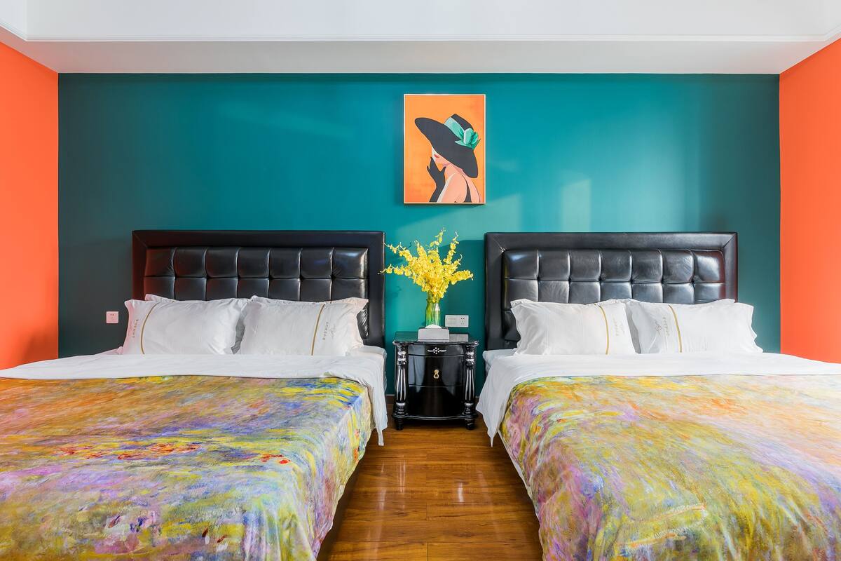 A hotel room with two beds, teal walls, and a painting of a woman in a hat.