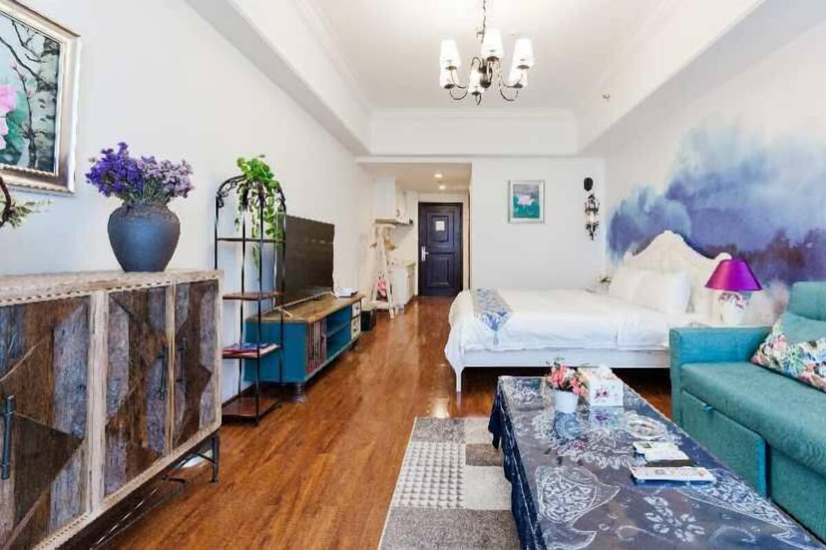 A living room with a bed, a sofa, a TV, a chandelier, and a wall with a painting.