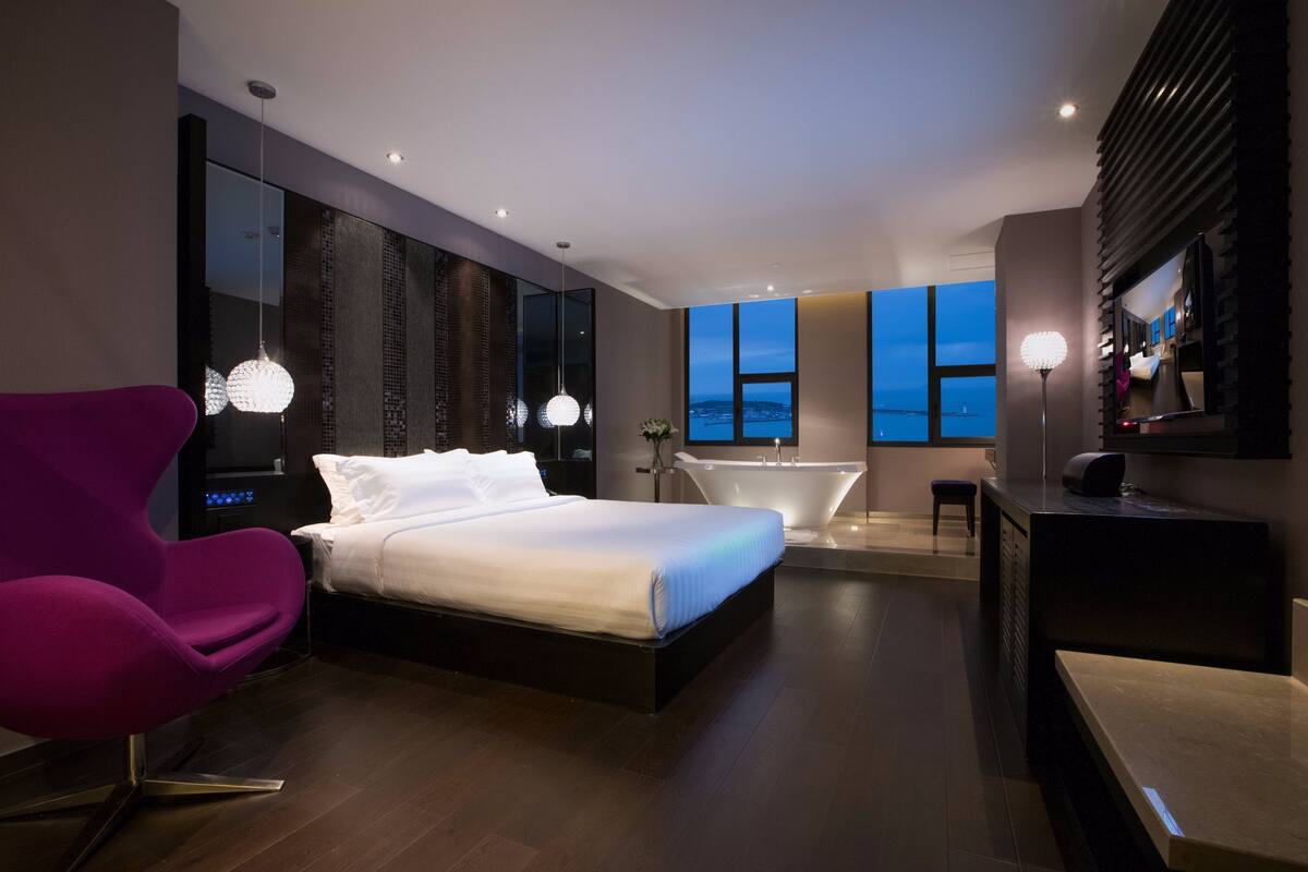 Un moderno cuarto de hotel con una cama grande, un tocador con espejo, una bañera y vistas a la ciudad.