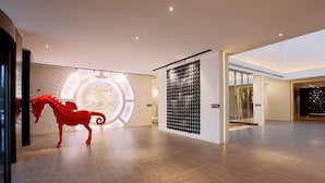 A spacious, modern interior with a wooden floor, a large circular light installation, and a wall-mounted display of black objects.