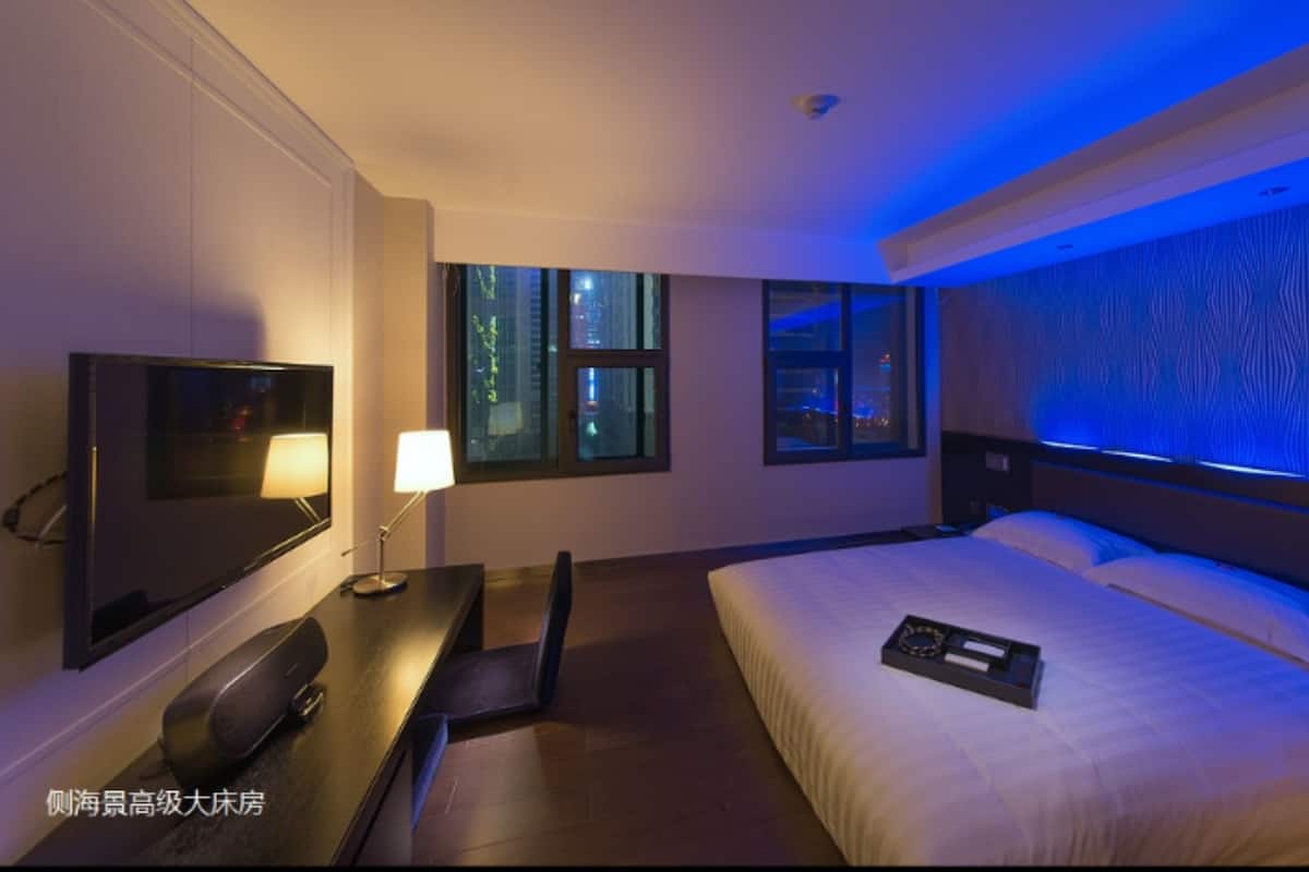 Habitación de hotel con cama, escritorio, televisión y ventana con vista a la ciudad de noche.