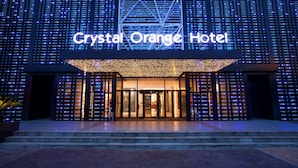 The exterior of the Crystal Orange Hotel with a prominent illuminated sign, a modern facade, and a set of double doors.