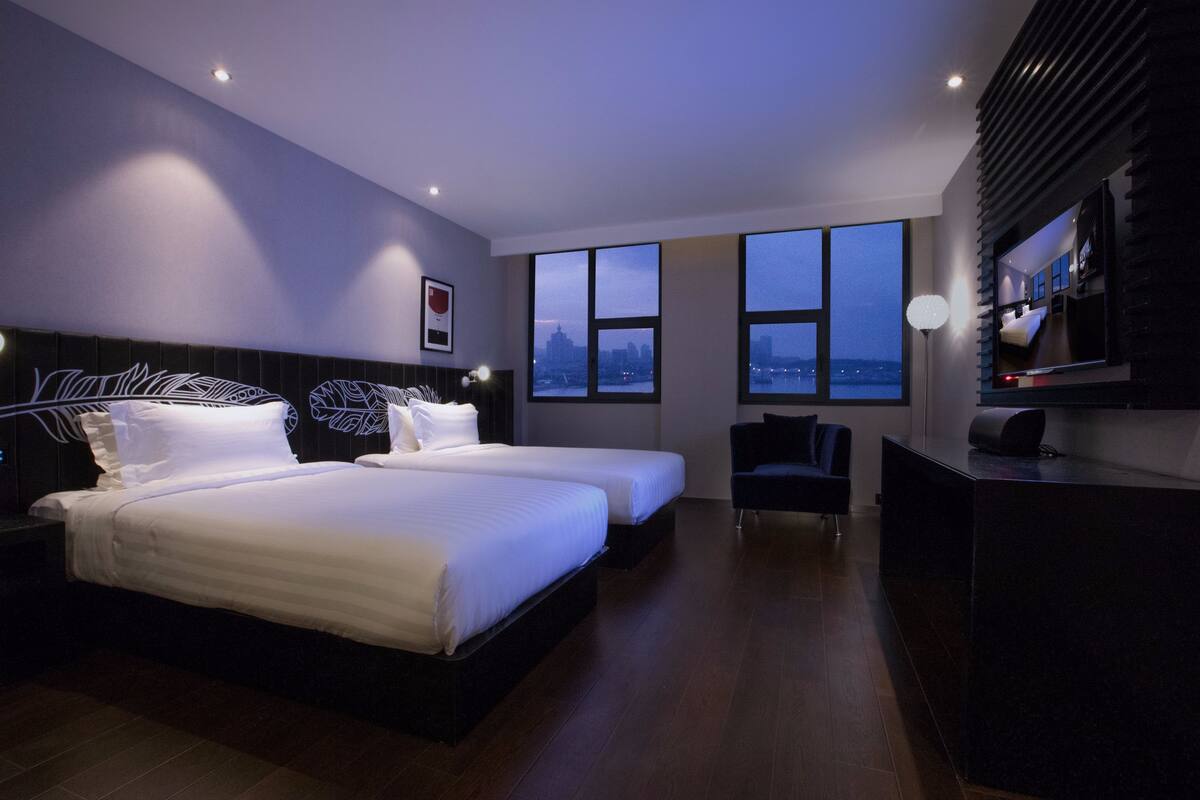 Una habitación de hotel moderna con dos camas, un escritorio y un amplio ventanal con vistas a la ciudad.