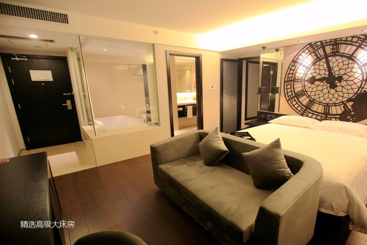 Una habitación de hotel con una cama grande, un sofá, una bañera y un reloj de pared.