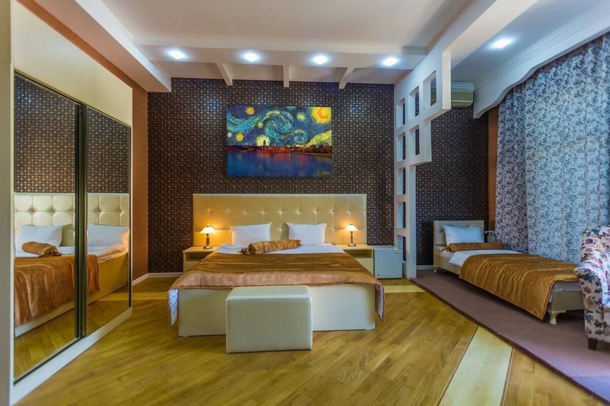 A hotel room with a large bed, a smaller bed, a sofa, a mirror, and a painting on the wall.