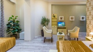 Un saló modern amb un sofà, dos butaques, una taula de centre i una televisió. Hi ha plantes i quadres a la paret.