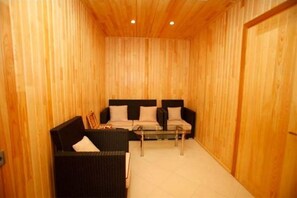 A wooden-paneled room with a black sofa, a smaller black chair, and a glass coffee table.