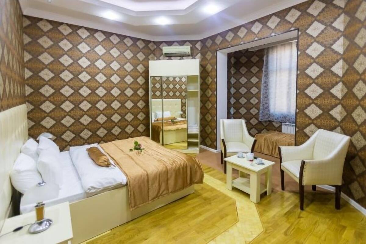 A hotel room with a bed, bedside table, two chairs, a small table, and a wardrobe.