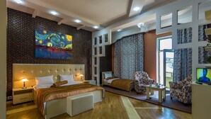 Habitació d'hotel moderna amb un llit gran, una zona d'estar amb un sofà i butaques, una televisió i un quadre gran a la paret.