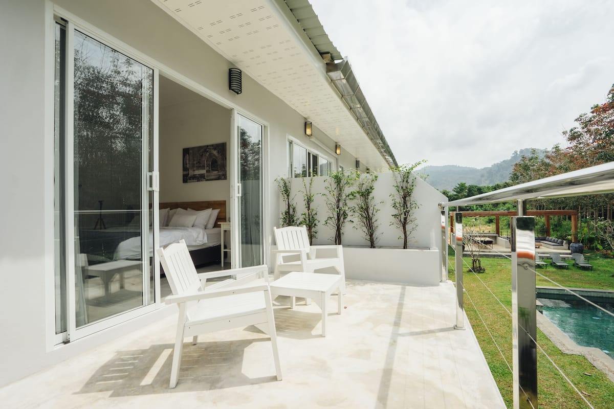 Eine moderne Außenpatio mit weißer Möbel, eine Glastür, die zu einem Schlafzimmer führt, und ein Poolbereich im Hintergrund.
