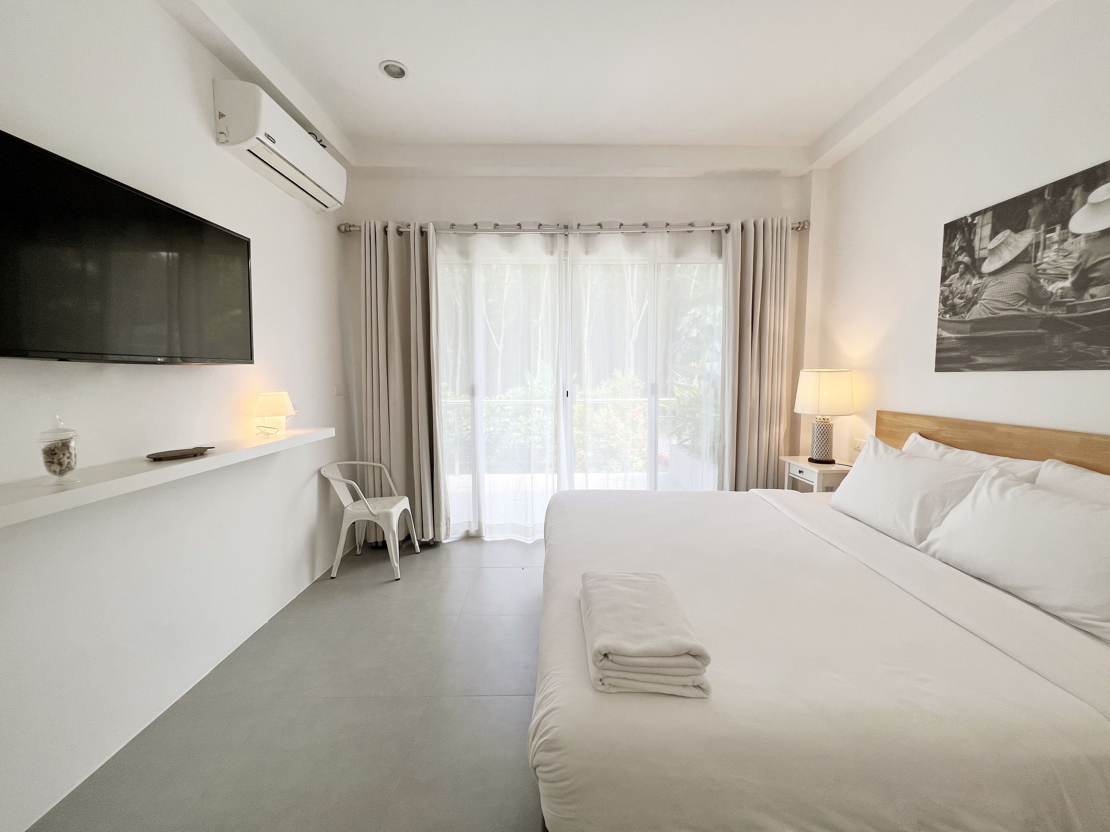 Habitación de hotel con cama, televisión montada en la pared, silla, lámpara y ventana con cortinas.