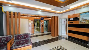 Un hall d’hôtel comprenant un comptoir d’accueil, un canapé à motifs, un espace d’accueil en bois et un ascenseur.