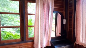 Una habitación de madera con ventana, cortinas, un espejo y un escritorio pequeño con cajones.