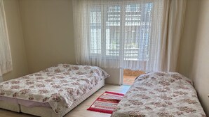 A bedroom with two single beds, a window with sheer curtains, and a patterned rug on the floor. - Amasra Seçil Günlük Kiralık Daire  (Amasra)
