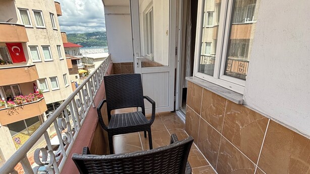 A balcony with two wicker chairs, a metal railing, and a view of a cityscape. - Amasra Seçil Günlük Kiralık Daire  (Amasra)