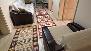 A small, well-lit room with a sofa, a TV, a small table, and a patterned rug. - Amasra Seçil Günlük Kiralık Daire  (Amasra)