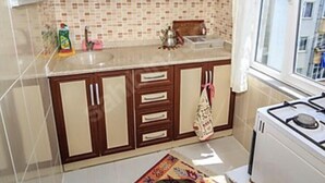 A kitchen with wooden cabinets, a tiled backsplash, a stove, and a window. - Amasra Seçil Günlük Kiralık Daire  (Amasra)