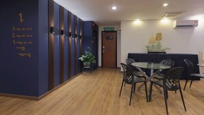 A hotel lobby with a reception desk, a seating area with a glass table and chairs, and a wall with room numbers and directional signs. - Chimera Hotel (Kota Kinabalu)