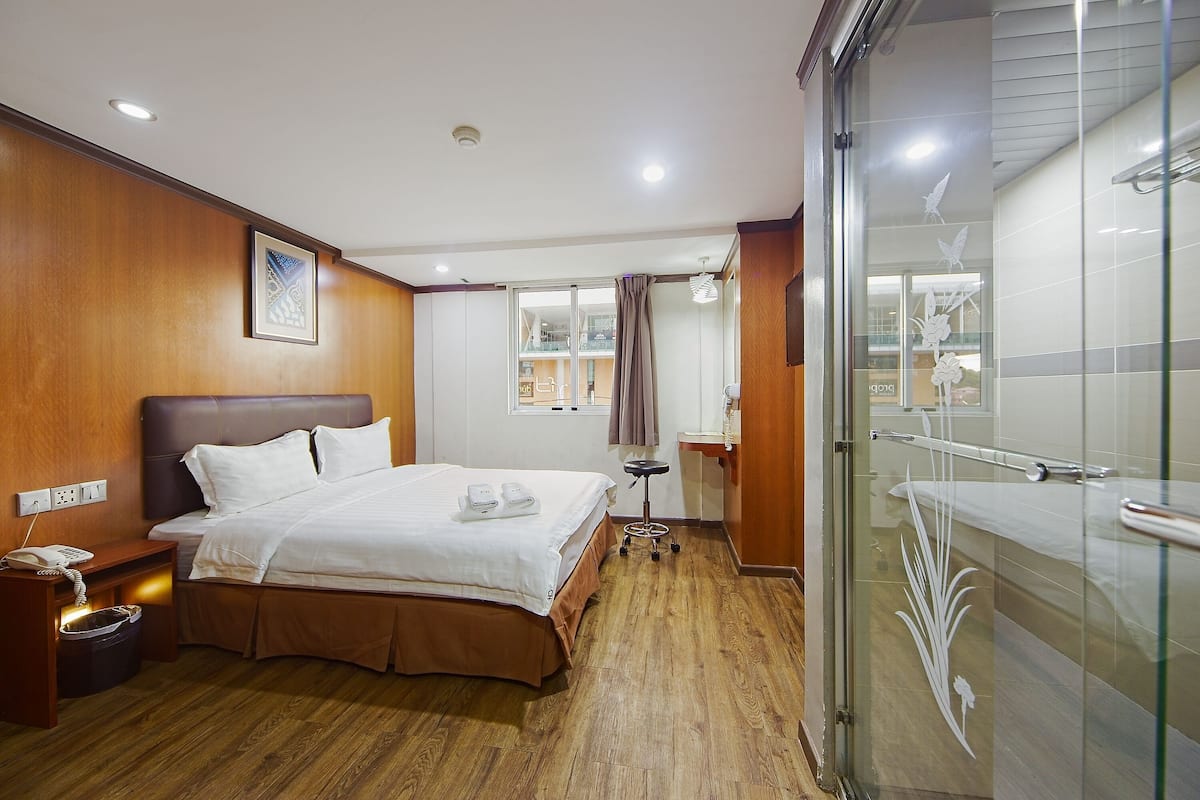 A hotel room with a bed, bedside table, and a glass-enclosed shower area.