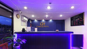 A hotel reception desk with a clock, a digital display board, and a potted plant. - Chimera Hotel (Kota Kinabalu)