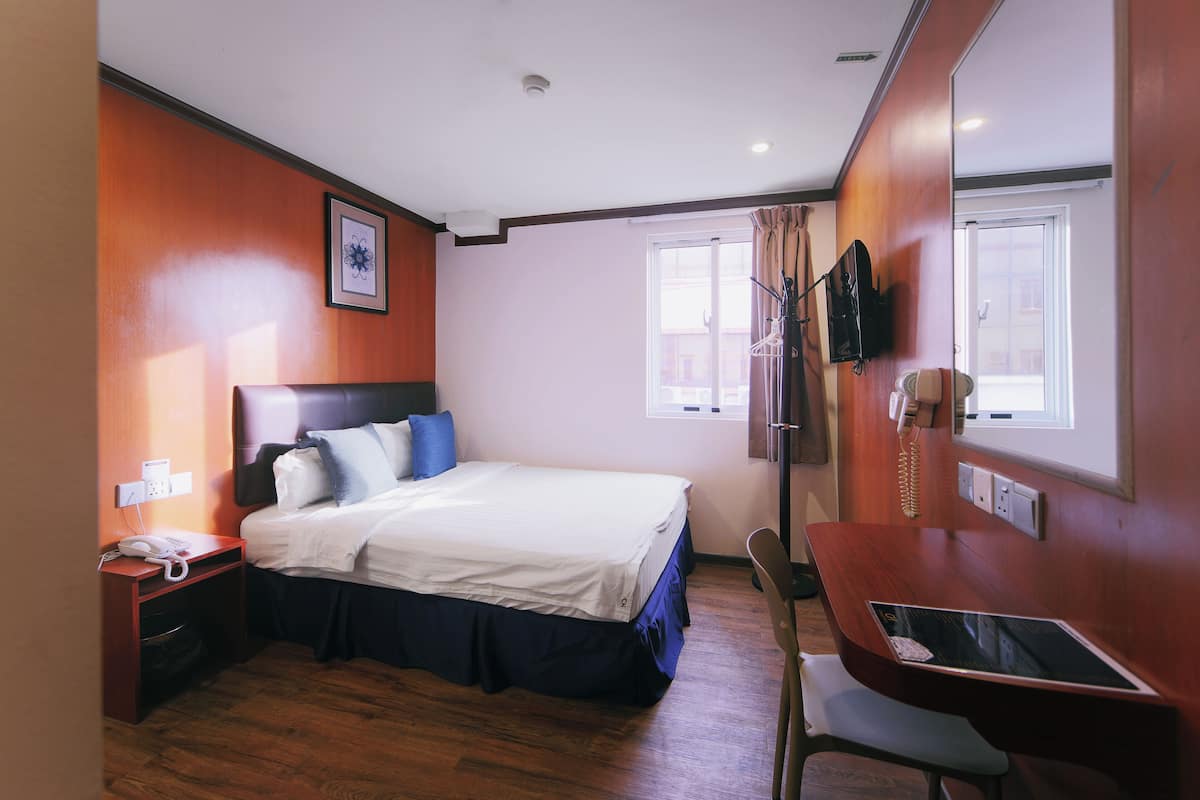 A hotel room with a bed, bedside table, desk, chair, and a window.