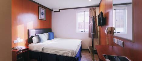 A hotel room with a bed, bedside table, desk, chair, and a window.