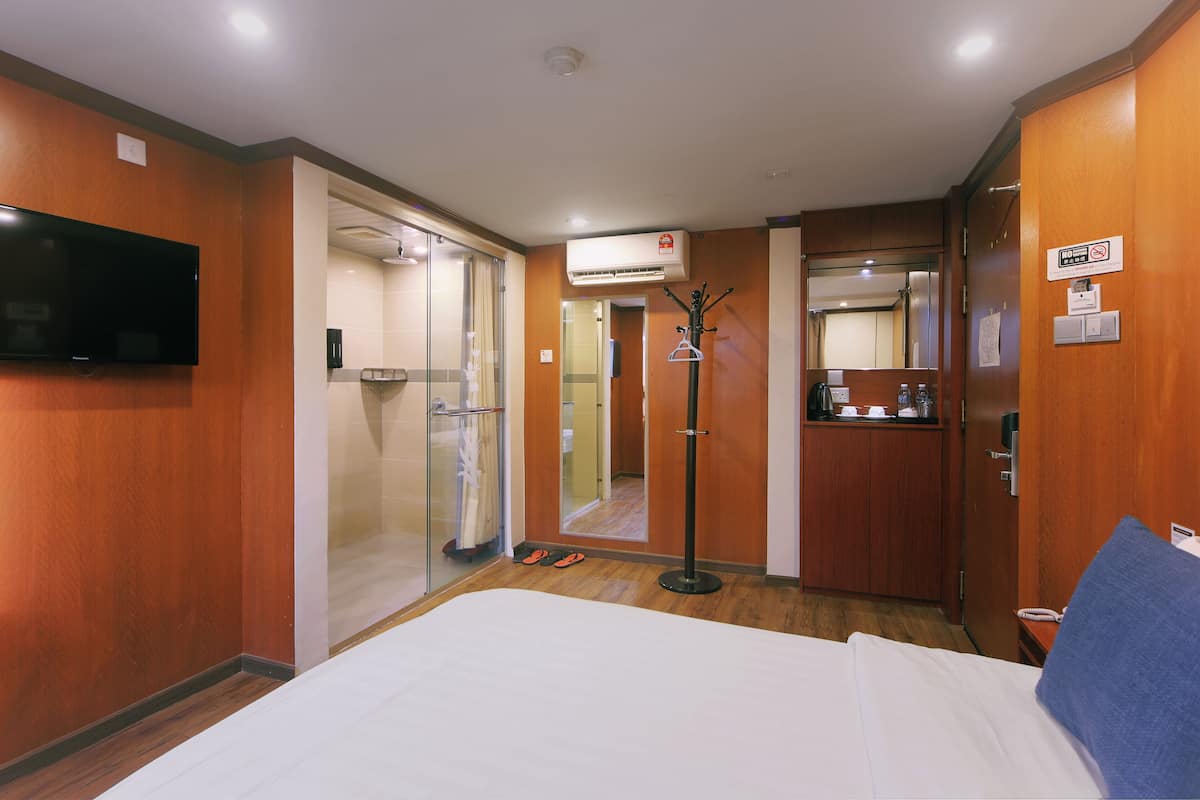 A hotel room with a bed, a TV, a wardrobe, a mirror, and a bathroom visible through a glass door.