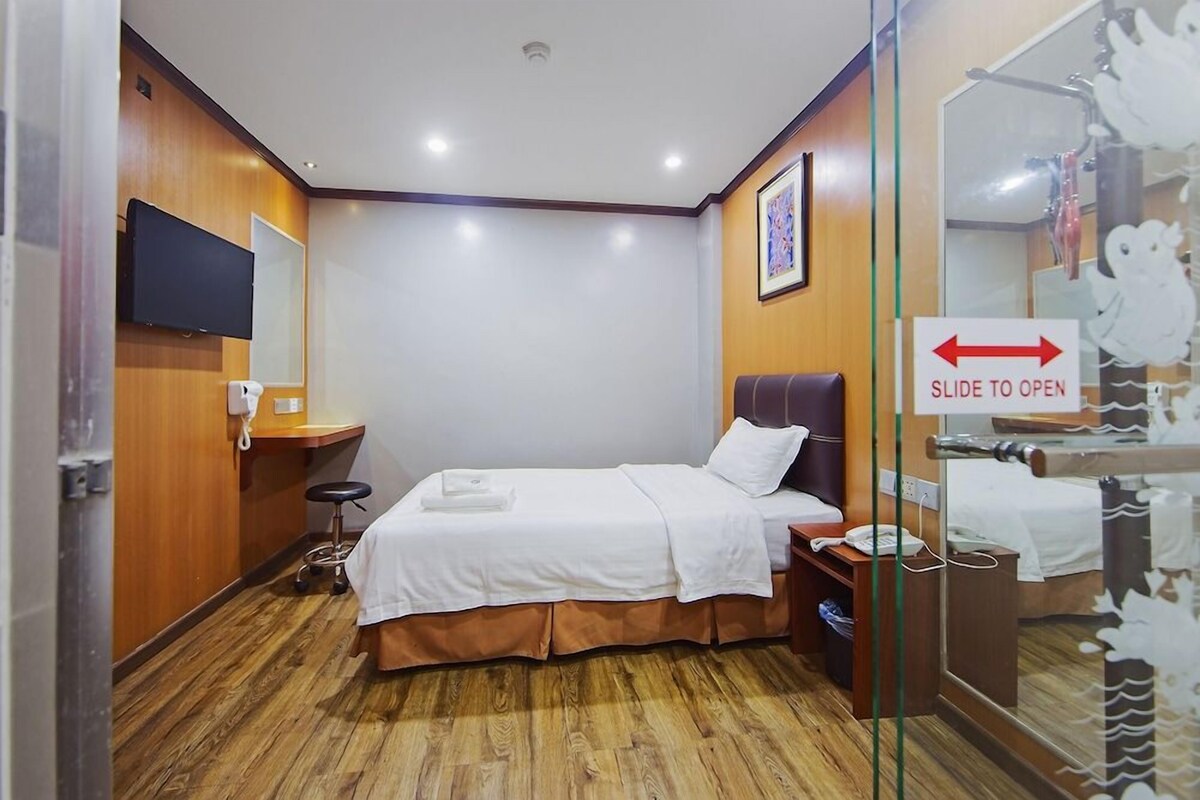 Una habitación de hotel con cama, escritorio, silla, televisor y espejo.