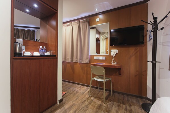 Ein Hotelzimmer mit einem Holzschrank, einem Schreibtisch mit Stuhl, einem Fernseher und einem Kleiderständer.