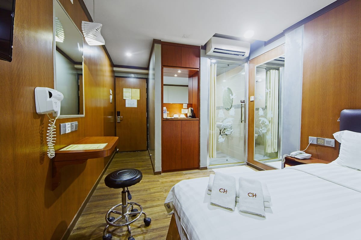 A hotel room with a bed, a desk, a mirror, a shower, and a bathroom.