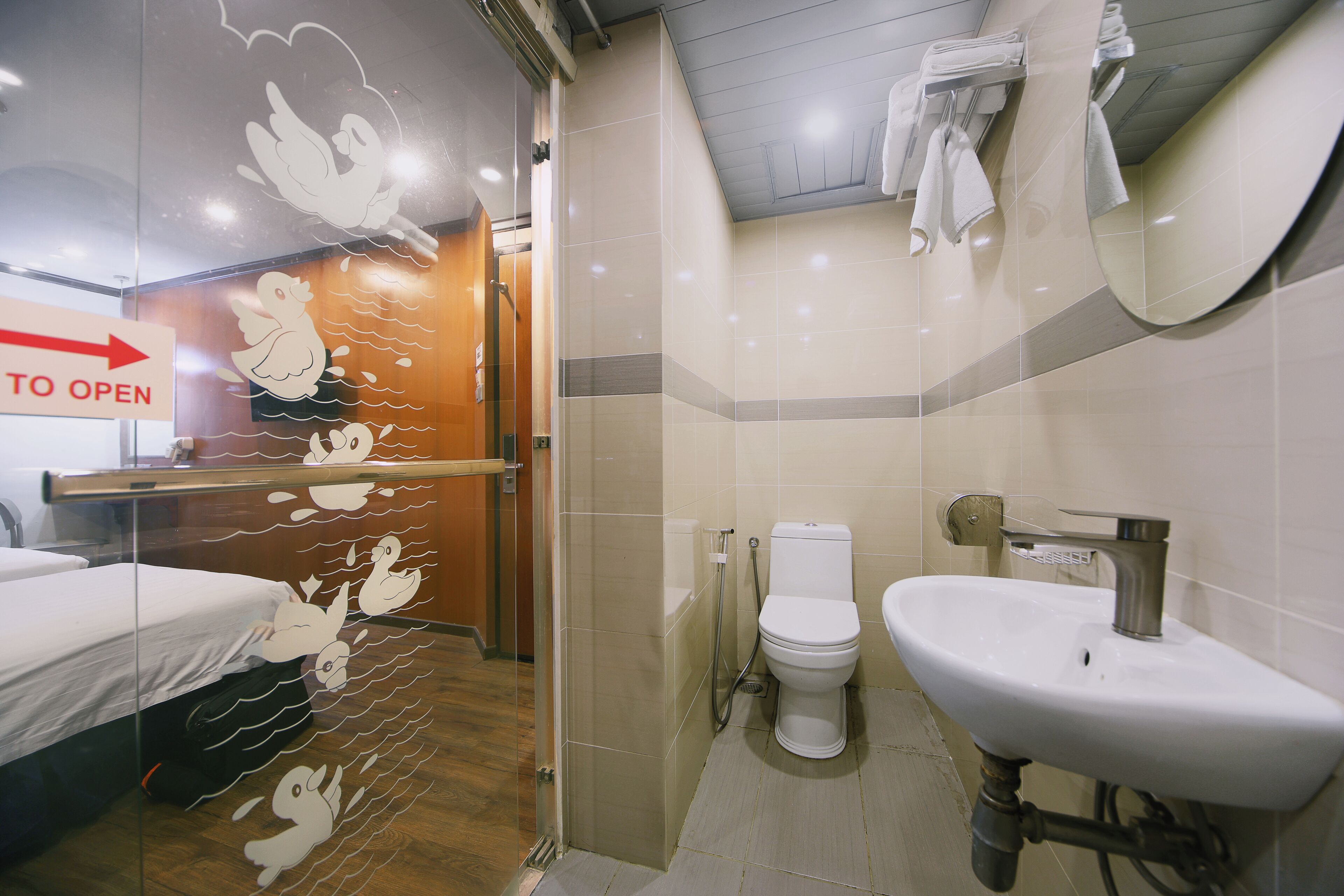 Ein Hotelbad mit Dusche, Toilette, Waschbecken und einem Bett mit Fensterdekor mit Entenmotiv.