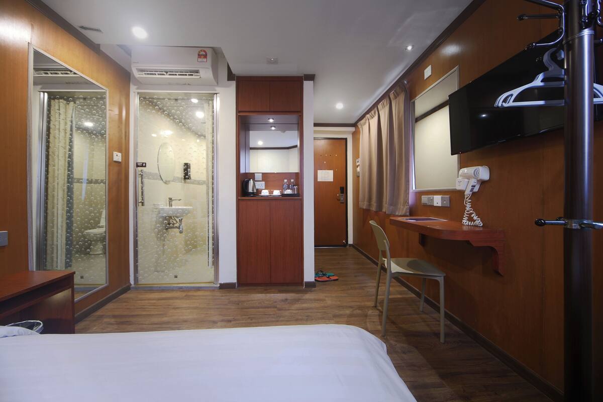 A hotel room with a bed, a shower, a sink, a mirror, and a TV mounted on the wall.