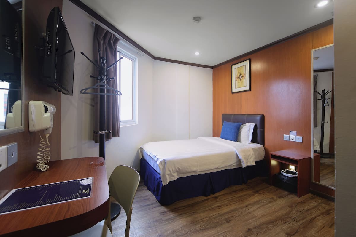 A hotel room with a bed, a desk with a telephone, a chair, a coat rack, and a mirror.