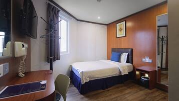 A hotel room with a bed, a desk with a telephone, a chair, a coat rack, and a mirror.