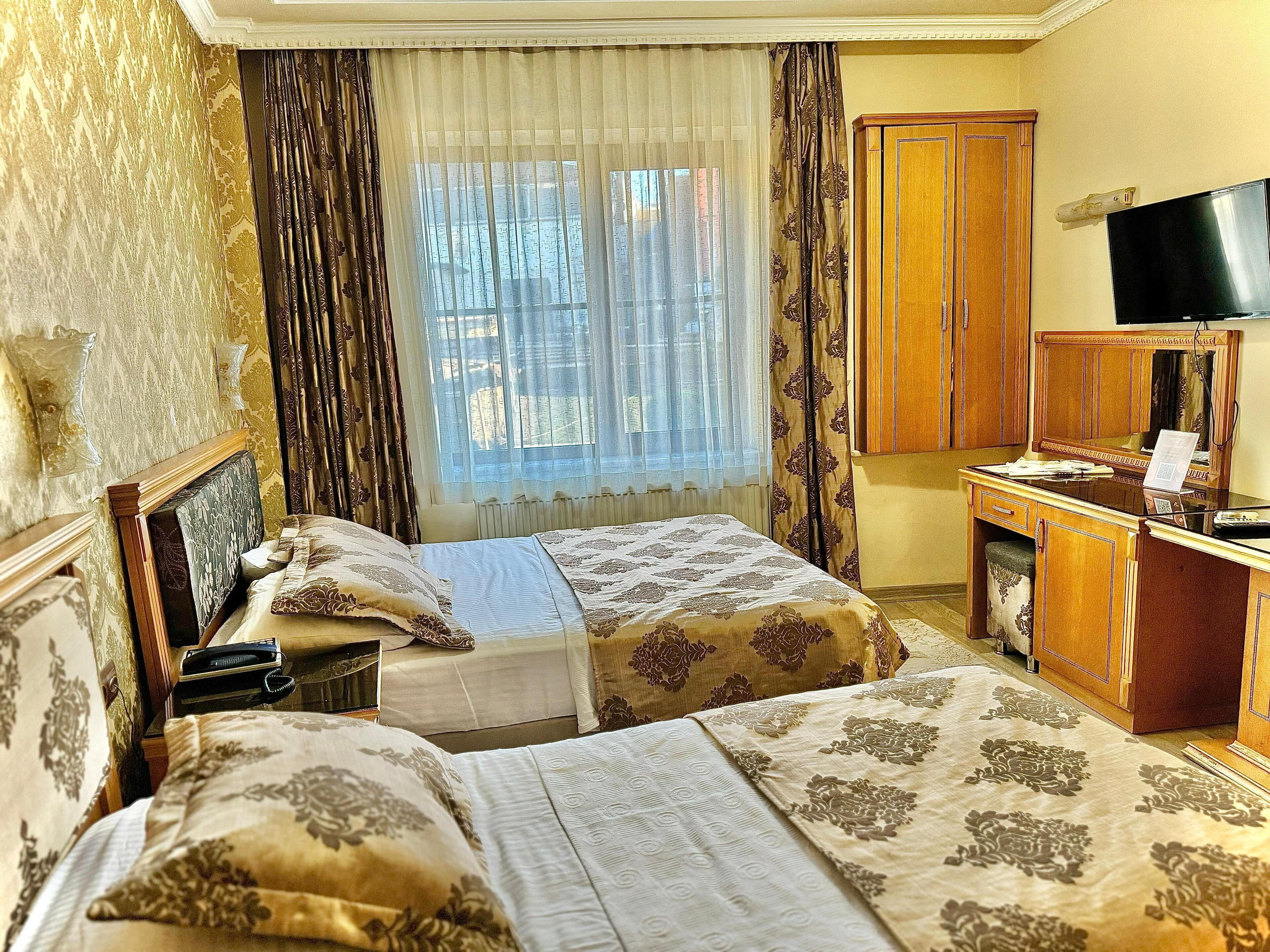 Une chambre d’hôtel avec deux lits, un bureau, une télévision et une fenêtre avec des rideaux.