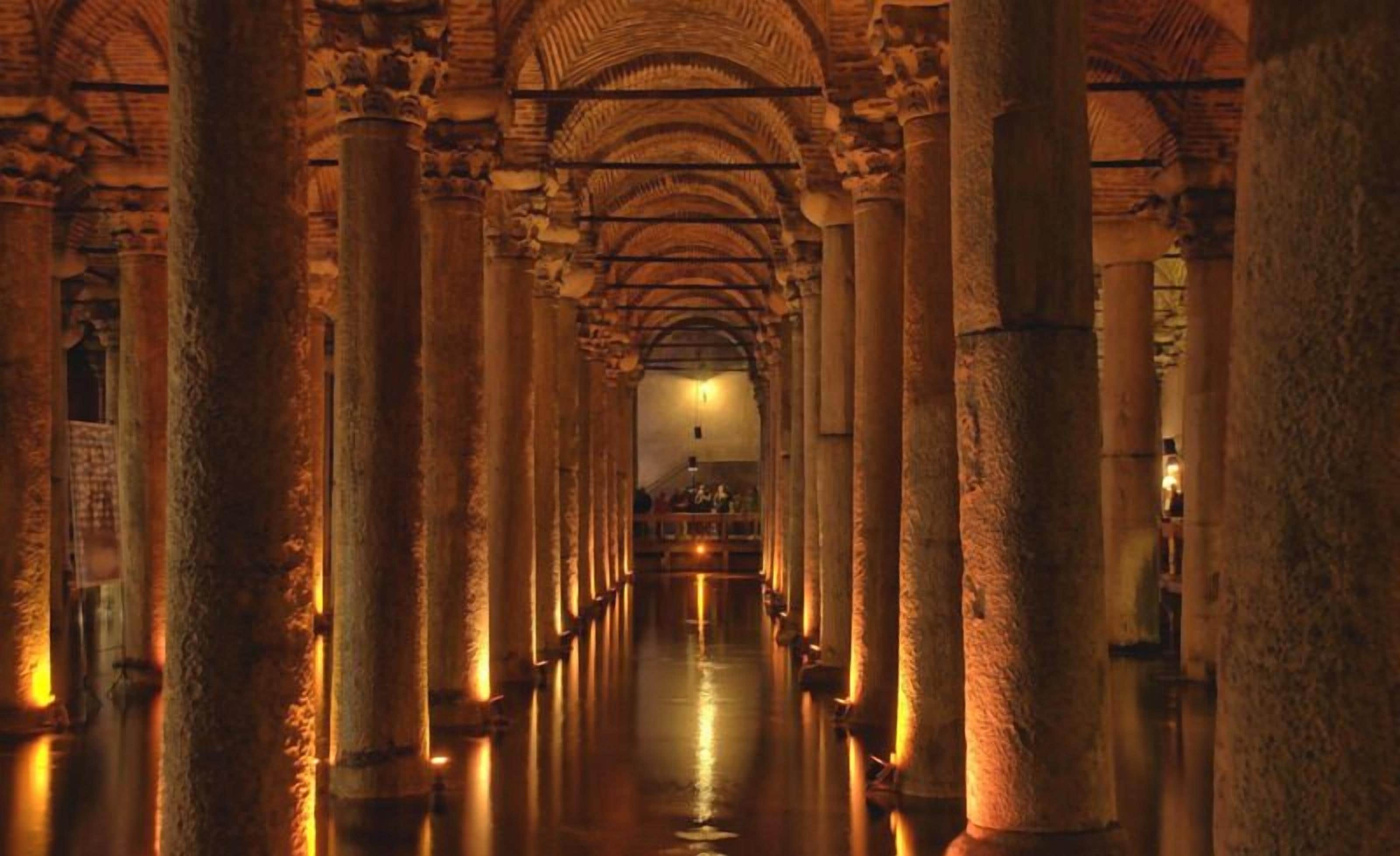 A corridor with high, arched ceilings and large columns, leading to a lit area at the end.
