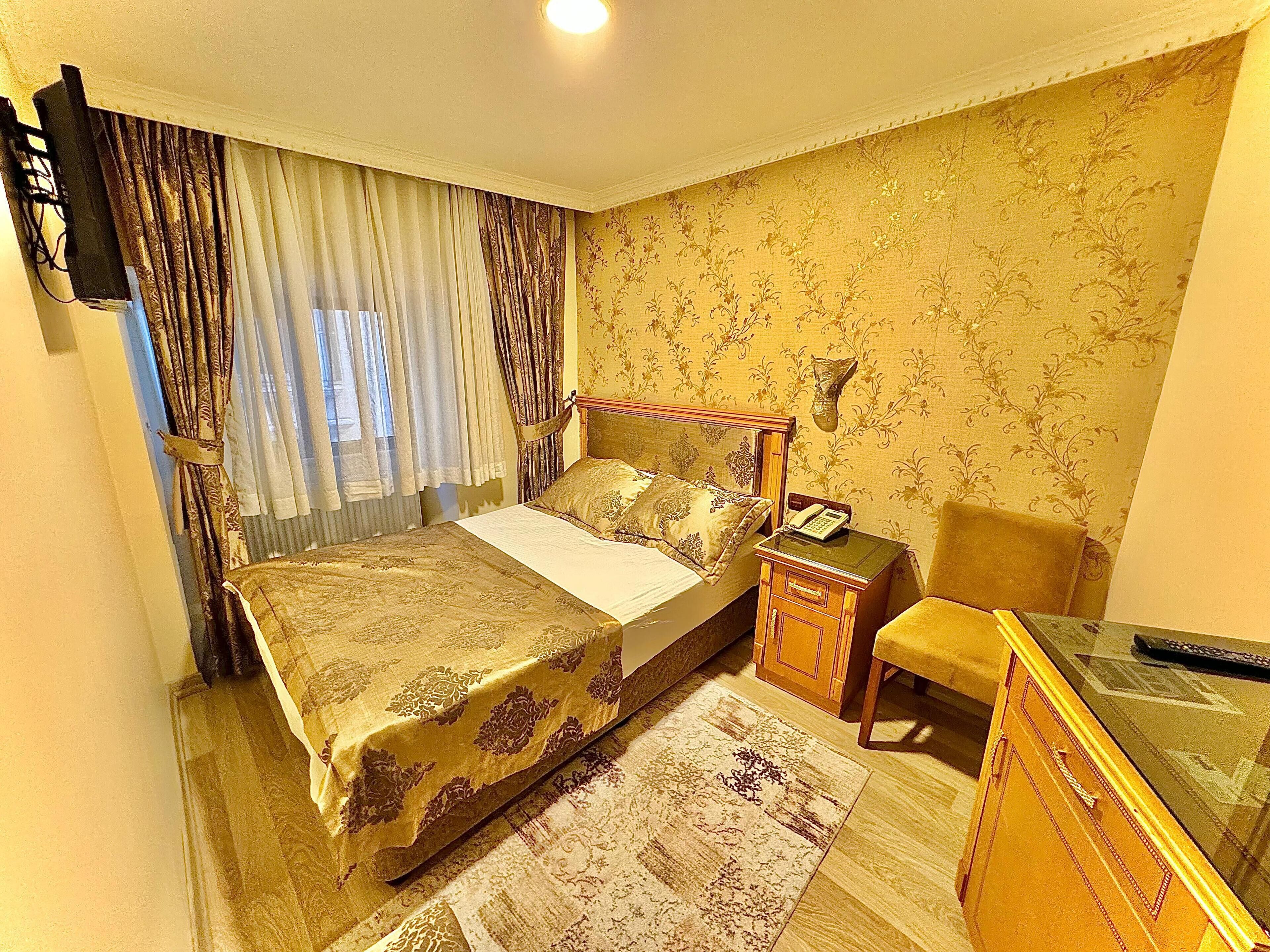 A hotel room with a bed, bedside table, chair, and a desk with a telephone.