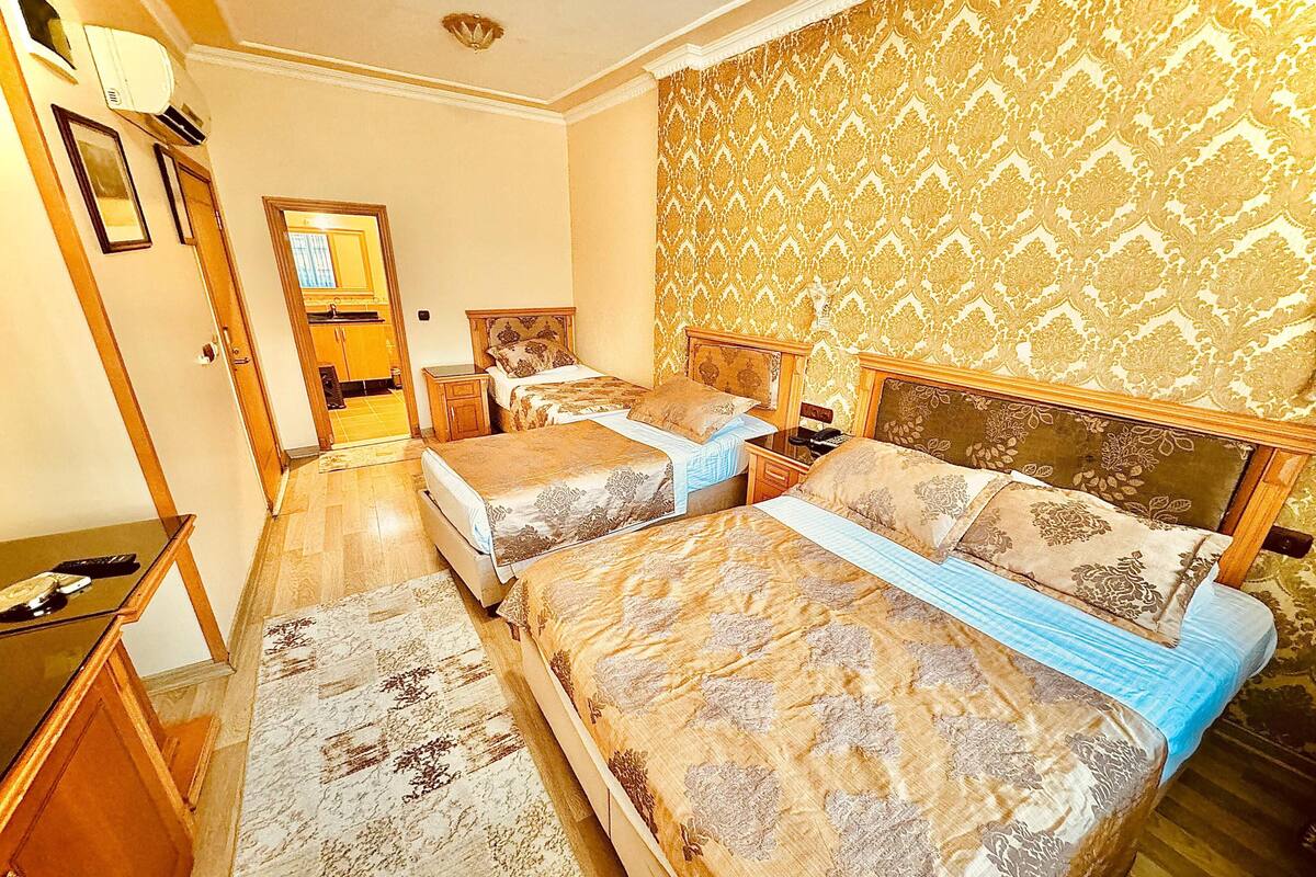 A hotel room with two beds, a desk, a chair, a mirror, and a patterned wallpaper.