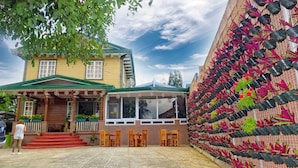 A building with a green roof and a porch with wooden chairs. - Elmar Cabin (Baguio)