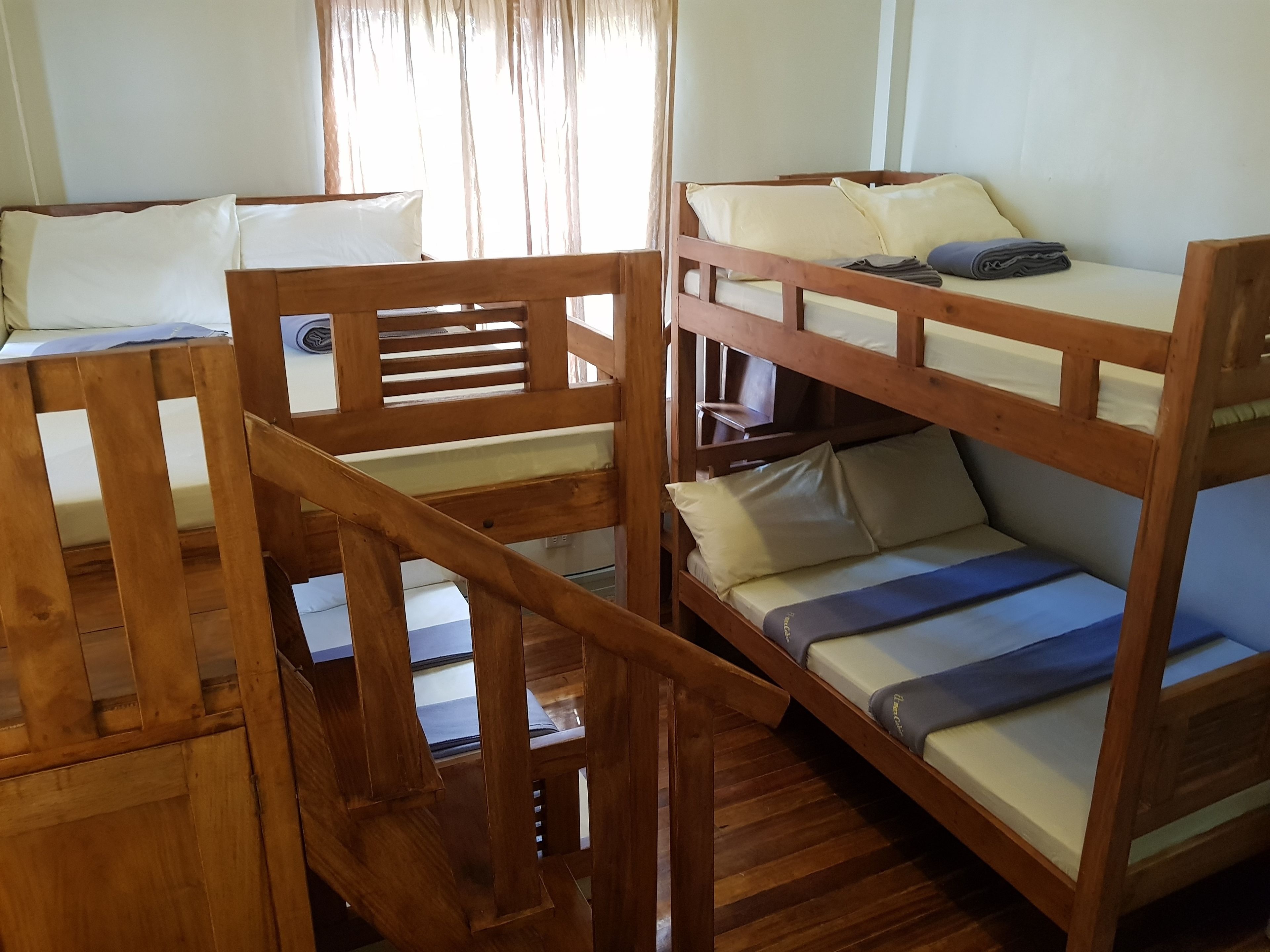 Habitación con literas, barandales de madera y una ventana con cortinas.