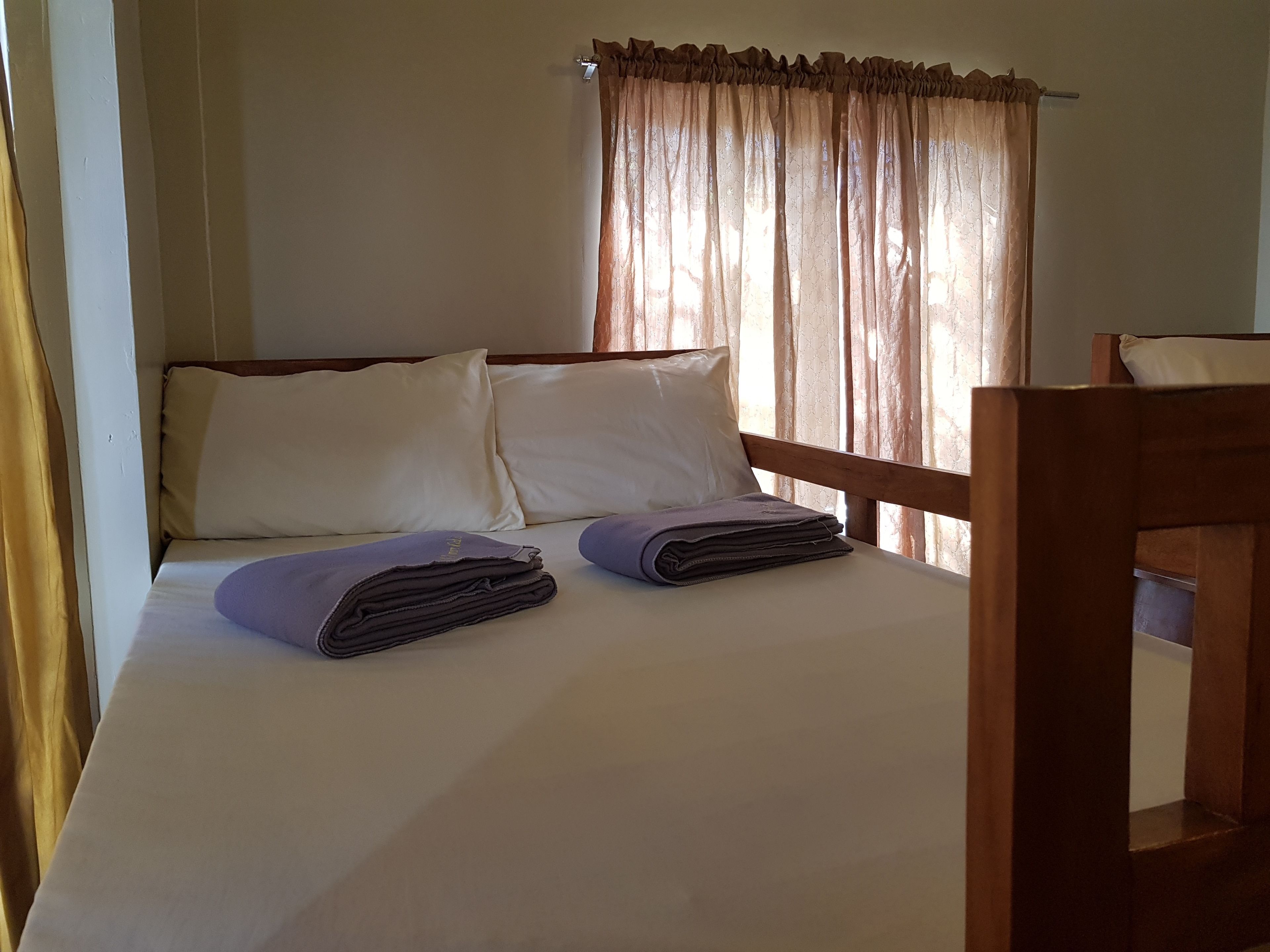 Una cama con sábanas blancas, dos almohadas y toallas dobladas.